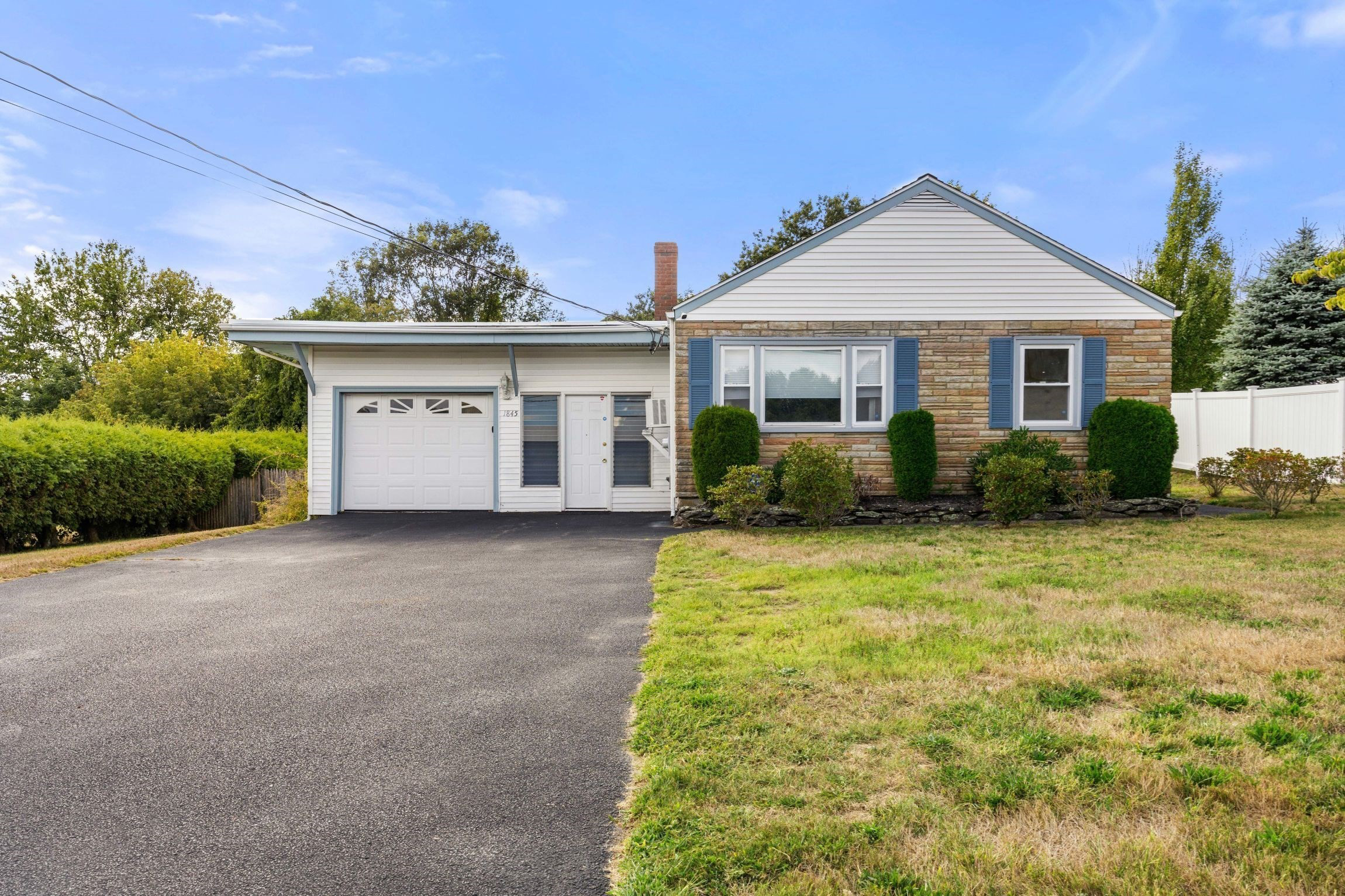 Front view of 1845 Main Street in Brockton showcasing ranch-style home with attached garage and manicured shrubs.