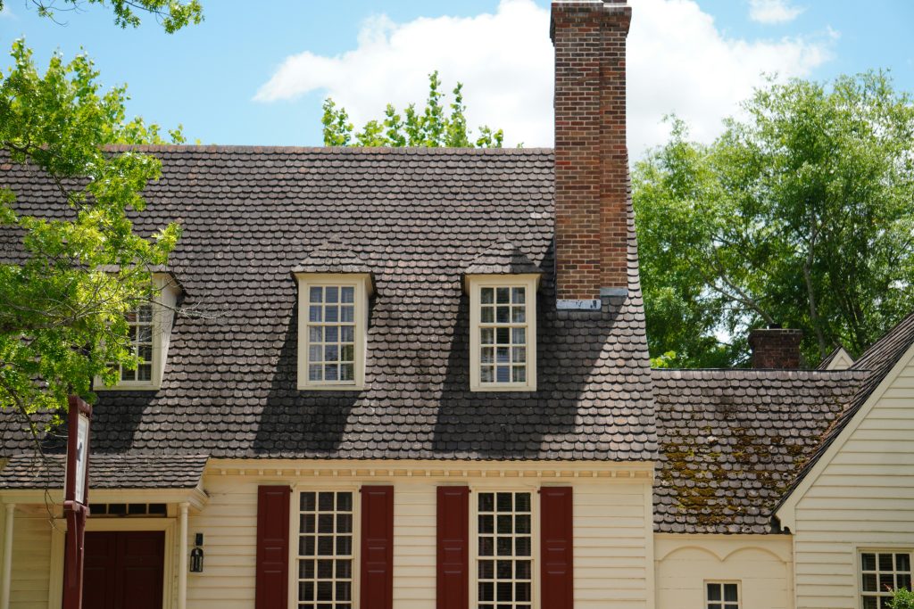 A close-up view of a home’s rooftop showing aging shingles, moss growth, and a brick chimney under bright daylight—illustrating potential warning signs a roof may be vulnerable before winter.